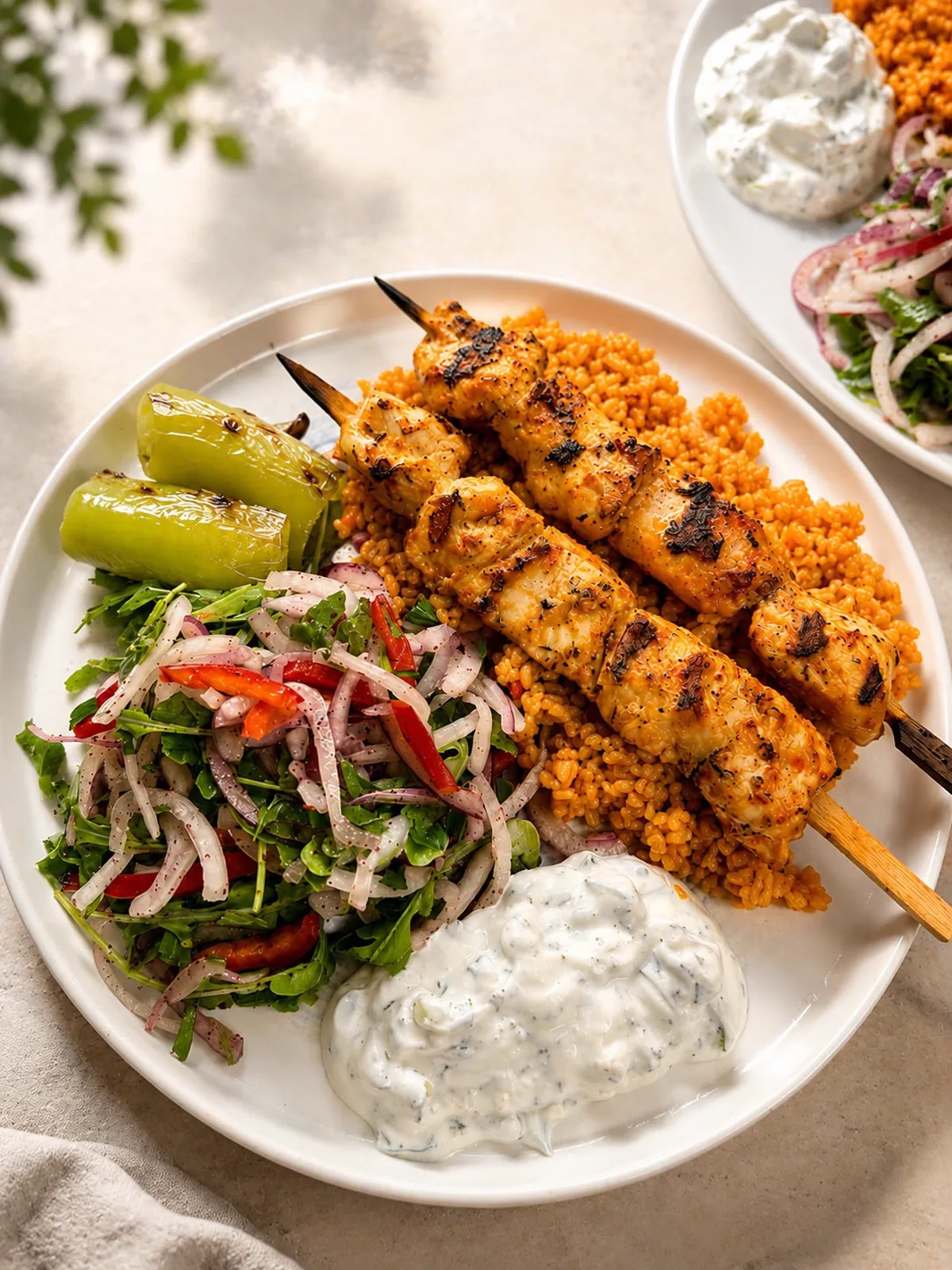 Zwei Hähnchenspieße vom Holzkohlegrill auf Bulgur, dazu Sumak-Zwiebelsalat, gegrillte Peperoni und Cacık